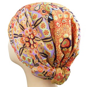 May include: A colorful head wrap featuring a vibrant floral pattern in shades of orange, purple, yellow, and brown. The fabric is knotted at the base, creating a stylish and functional accessory. This head wrap is designed to be worn on the head.