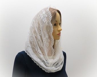 May include: A white lace veil with a floral pattern. The veil is draped over a mannequin's head and shoulders, showcasing its delicate design and scalloped edges. The fabric appears soft and lightweight, suitable for special occasions.