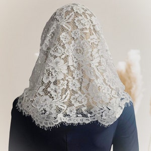 May include: A white lace veil with a floral pattern. The veil is draped over a person's head and shoulders.