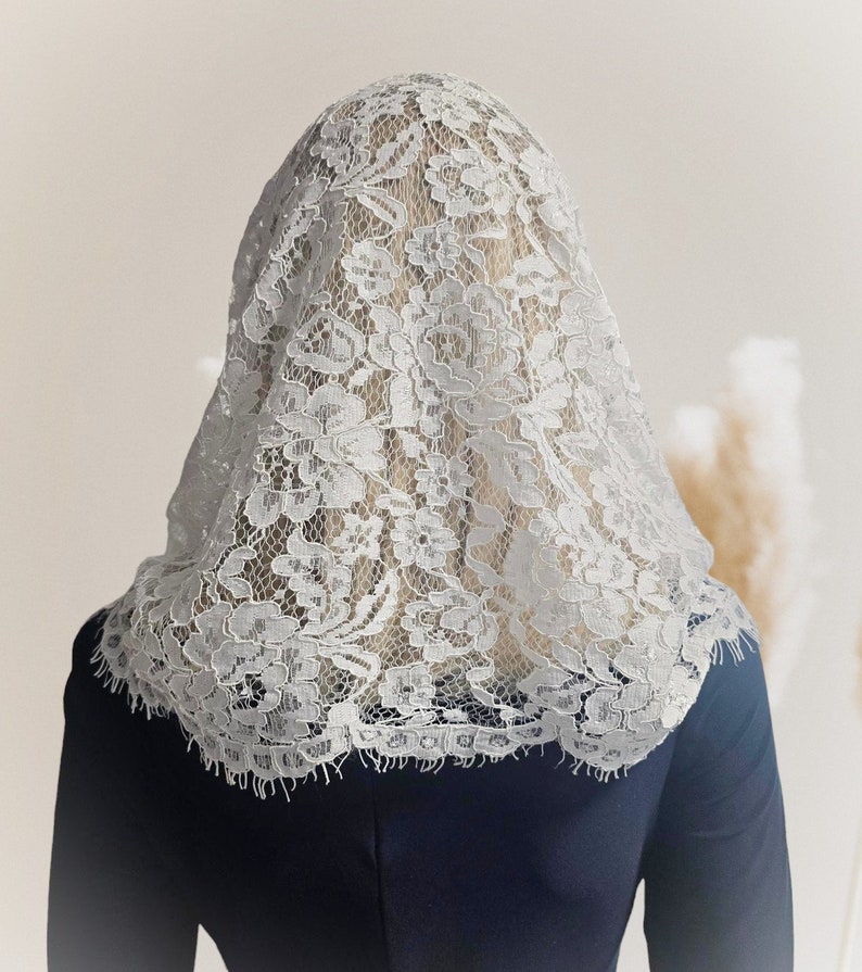 May include: A white lace veil with a floral pattern. The veil is draped over a person's head and shoulders.