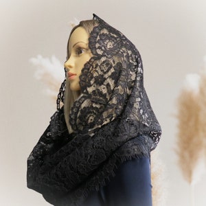 May include: A black lace mantilla with a delicate floral pattern. The mantilla is draped over a mannequin's head and shoulders.