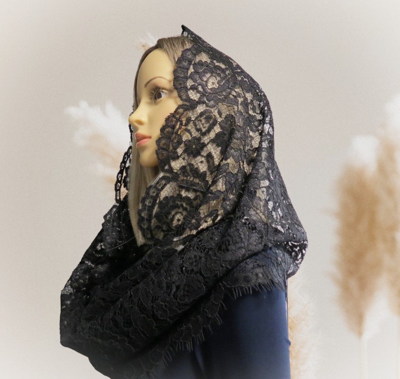 May include: A black lace mantilla with a delicate floral pattern. The mantilla is draped over a mannequin's head and shoulders.