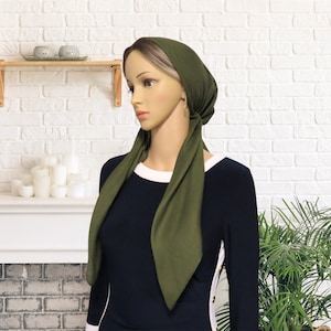 Puede incluir: Un pañuelo de cabeza verde con lazos largos. El pañuelo está atado alrededor de la cabeza y los lazos cuelgan hacia abajo en la parte delantera del cuello. El pañuelo está hecho de una tela suave y elástica.