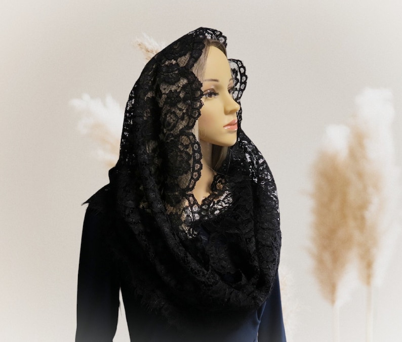 May include: A black lace mantilla, a traditional head covering, draped over a mannequin's head. The lace is delicate and intricate, with a floral pattern.