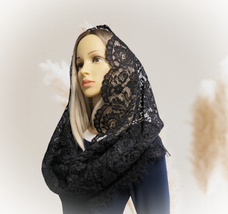 May include: A black lace mantilla with a scalloped edge. The mantilla is draped over a mannequin's head and shoulders.