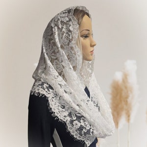 May include: White lace mantilla with a delicate floral pattern. The mantilla is draped over a mannequin's head and shoulders.