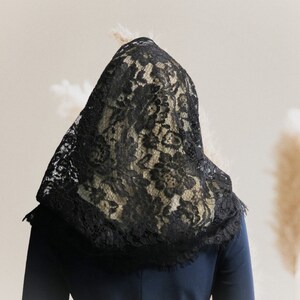 May include: A black lace veil covers the head and shoulders of a person wearing a dark blue shirt.