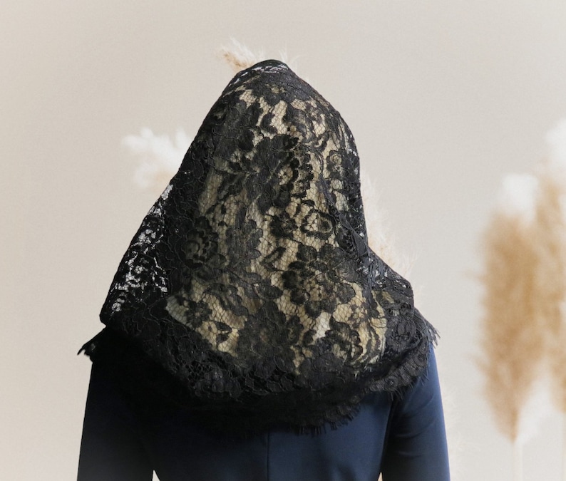 May include: A black lace veil covers the head and shoulders of a person wearing a dark blue shirt.