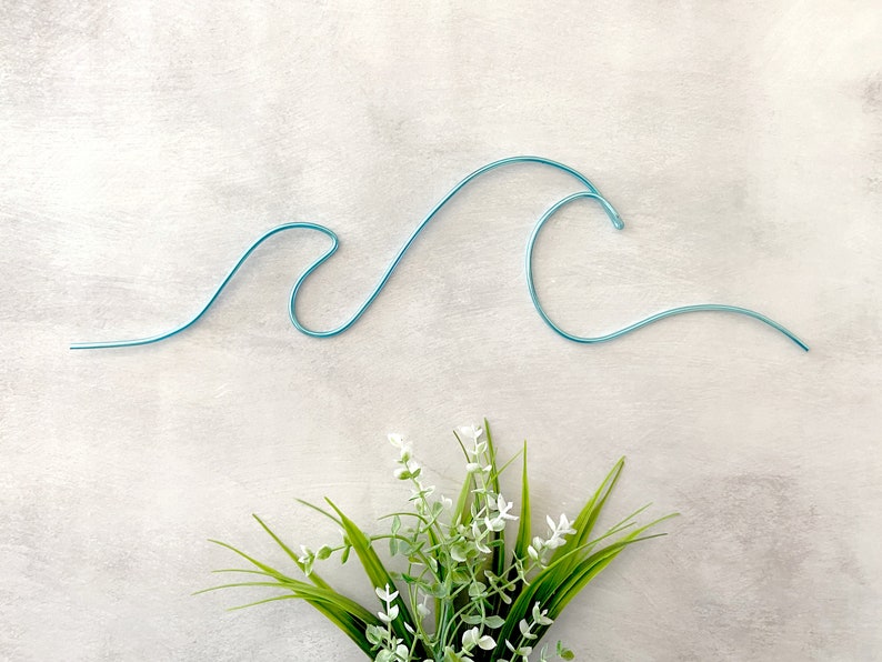 May include: A blue wire wave sculpture with a small green plant with white flowers in the bottom center of the image.
