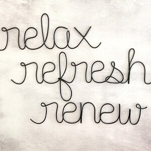 Puede incluir: Escultura de alambre negro con las palabras "relax refresh renew" sobre un fondo blanco.