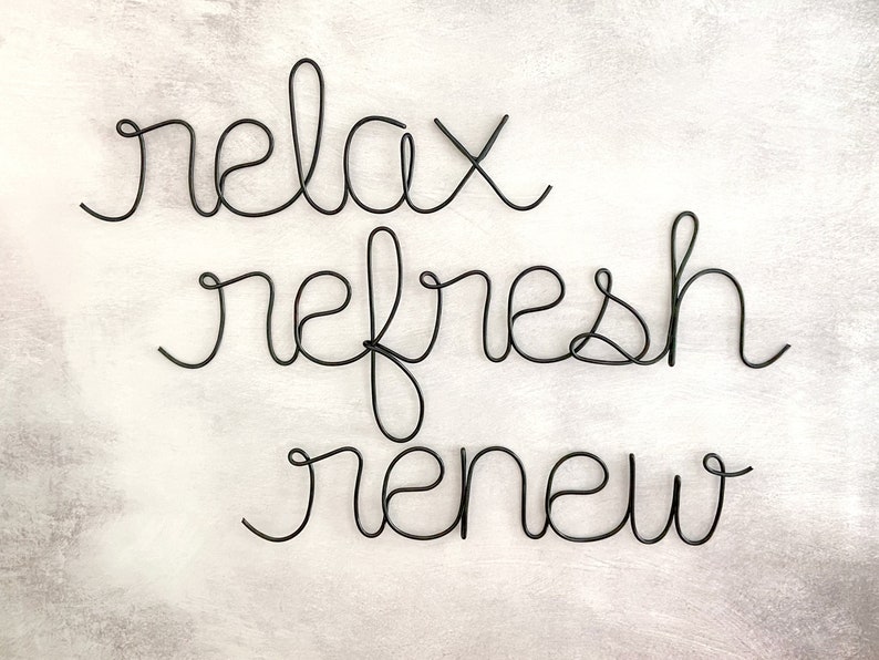 Puede incluir: Escultura de alambre negro con las palabras "relax refresh renew" sobre un fondo blanco.