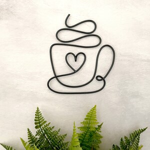 Puede incluir: Escultura de alambre negro de una taza de caf&eacute; con un coraz&oacute;n en el centro. La taza tiene un dise&ntilde;o de espiral en la parte superior, que representa crema batida.