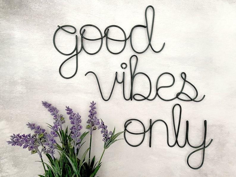 May include: Black wire sculpture on a white background with the words "good vibes only" and a bouquet of lavender flowers in the bottom left corner.