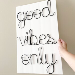 May include: A white background with black wire lettering that reads "good vibes only".
