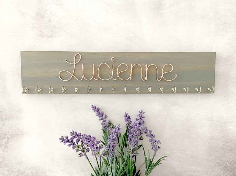 May include: A handcrafted wooden 'Welcome' sign in a whimsical font. The white-painted sign has a distressed finish and a floral design in pinks and greens. Suitable for indoor or outdoor display.