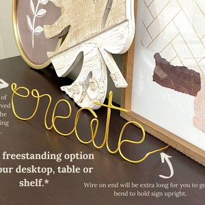 May include: Gold wire word art spelling "create" with a curved wire on one end for freestanding display. The text "New freestanding option for your desktop, table or shelf." is written below the word art.