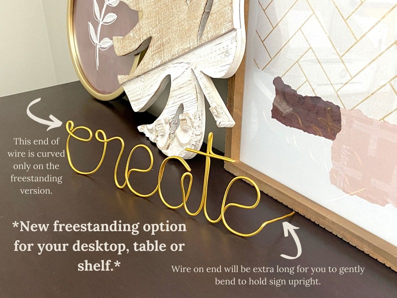 May include: Gold wire word art spelling "create" with a curved wire on one end for freestanding display. The text "New freestanding option for your desktop, table or shelf." is written below the word art.