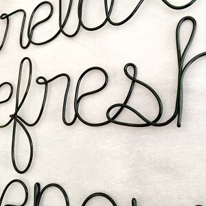 Puede incluir: Escultura de alambre de metal negro de las palabras "hello refresh" colgada en una pared blanca.