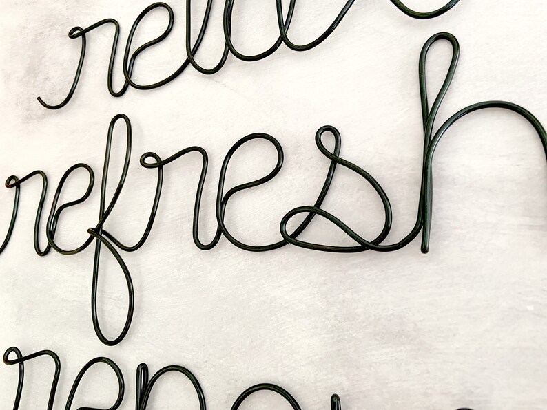 Puede incluir: Escultura de alambre de metal negro de las palabras "hello refresh" colgada en una pared blanca.