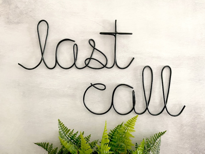 May include: Black metal wire sculpture of the words "last call" hanging on a white wall.