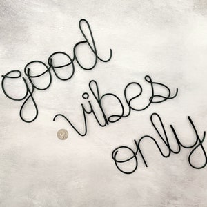 May include: Black wire wall decor with the words "good vibes only" in a cursive font.