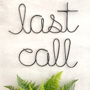 May include: Black metal wire sculpture of the words "last call" on a white background.