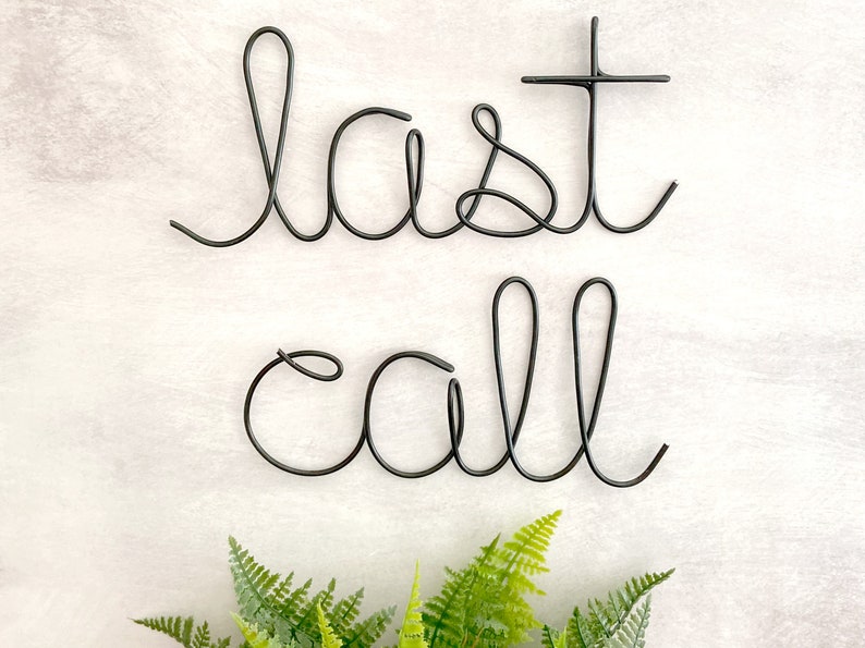May include: Black metal wire sculpture of the words "last call" on a white background.