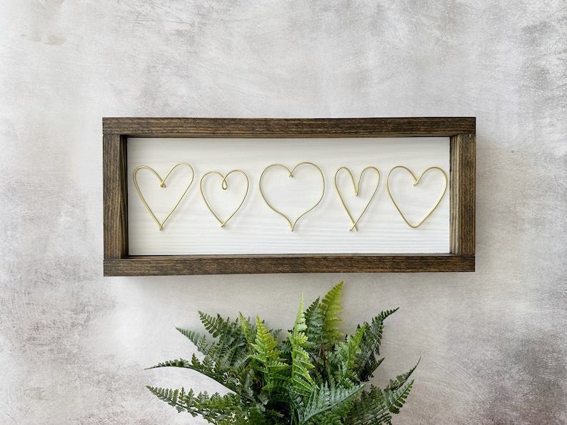 Custom hearts handcrafted from wire and attached on a white plank with a dark walnut frame.