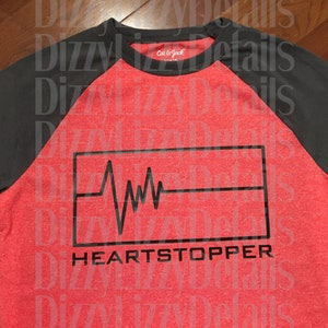 May include: Red and gray baseball tee shirt with a black graphic of a heartbeat and the text "HEARTSTOPPER".