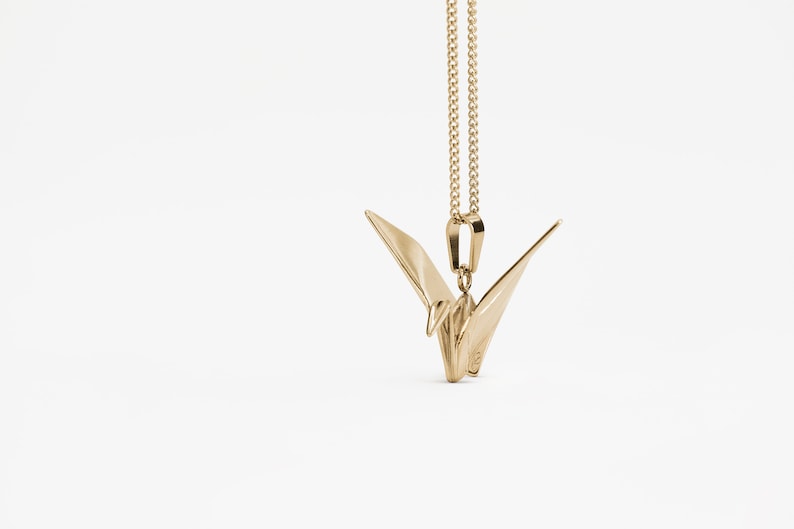 Peut inclure: Un collier avec un pendentif en forme de grue origami en or. La grue est un symbole de paix et de bonne chance.