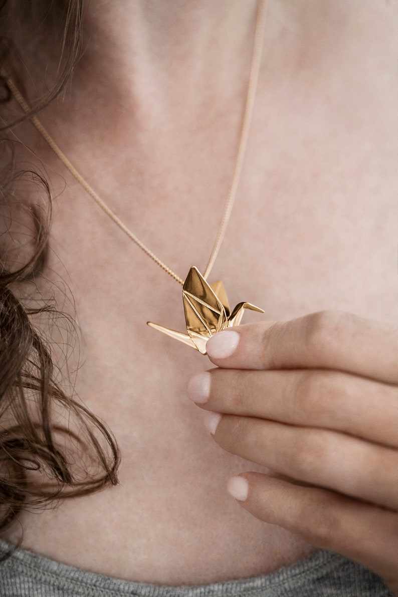 Peut inclure: Un collier avec un pendentif en forme de grue en origami dor&eacute;. La grue est un symbole de paix et de bonne chance.
