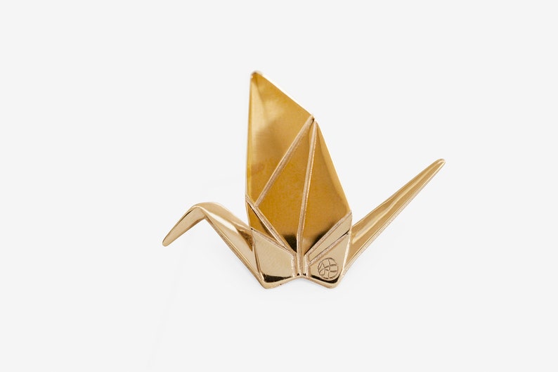 Peut inclure: Une sculpture de grue en origami dor&eacute;e. La grue est pli&eacute;e dans un style traditionnel et a un petit cercle avec un motif au centre de sa poitrine.