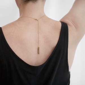 Peut inclure: Un collier en cha&icirc;ne dor&eacute;e avec un petit pendentif rectangulaire suspendu &agrave; l'arri&egrave;re du cou.