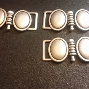 May include: Three silver metal clasps with oval-shaped closures. Each clasp has a decorative, textured, cylindrical piece in the center.