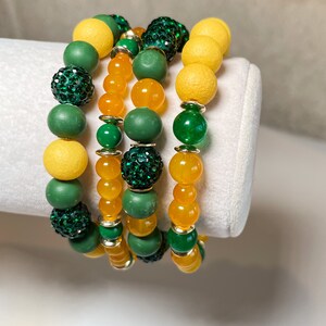 Może przedstawiać: Cztery bransoletki z zielonymi i żółtymi koralikami. Bransoletki mają okrągłe koraliki z błyszczącym zielonym wykończeniem.
