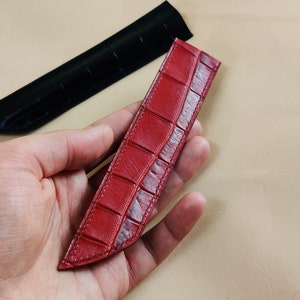 May include: A red leather pen holder with a crocodile pattern.