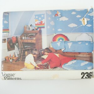 May include: A vintage sewing pattern for a children's bedroom set. The pattern includes instructions for making a bedspread, pillows, and a rainbow-shaped headboard. The pattern is illustrated with a photo of a child's bedroom with a blue and white bedspread, a rainbow headboard, and two children playing on the floor. The pattern number is 236.