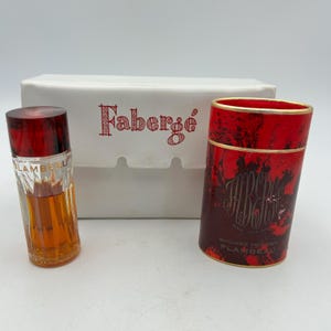 Könnte beinhalten: Ein Vintage-Faberge-Parfümset mit einer kleinen Glasflasche mit rotem Verschluss, einem zylindrischen Behälter in Rot und Braun sowie einer weißen Schachtel mit dem Faberge-Logo in Rot. Die Parfümflasche ist mit bernsteinfarbener Flüssigkeit gefüllt.