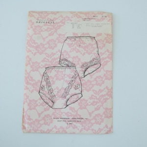 May include: A vintage sewing pattern for ladies' briefs. The pattern features line drawings of the briefs with floral lace detailing. The background is a pink floral lace pattern. The pattern is from Dolores of St. Paul.