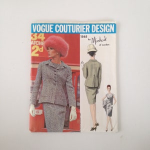 Könnte beinhalten: Vogue Couturier Design Schnittmuster Nummer 1565 von Michael of London. Das Schnittmuster zeigt zwei Frauen in verschiedenen Outfits. Eine Frau trägt einen grauen Tweed-Anzug mit einem rosa Hut. Die andere Frau trägt einen grünen Anzug mit einem weißen Hut.