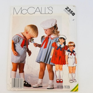 May include: A McCall's 2358 sewing pattern envelope for toddler clothing. The cover features illustrations of children wearing sailor-style outfits, including a light blue romper, a light blue pleated dress with a red tie, a red dress, and a white romper.
