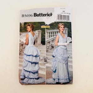 Op de afbeelding: Een Butterick B5696 naaipatroon-envelop met een lichtblauw mouwloos lijfje en een lange rok met een bustle-achterkant en een geplooide zoom. De voorzijde toont twee aanzichten van het kledingstuk, inclusief witte handschoenen en een waaier.