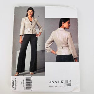 Puede incluir: Un sobre de patrón de costura para un conjunto Anne Klein Vogue American Designer que presenta un blazer beige claro con cintura anudada y mangas tres cuartos, combinado con pantalones negros de pierna ancha. El número V2896 es visible.