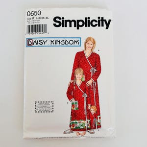 May include: A Simplicity Daisy Kingdom sewing pattern envelope 0650 for matching red wrap robes with white polka dots and Christmas stocking hem prints. The illustration shows an adult, a child, and a doll wearing the robes. Includes bonus doll pattern.