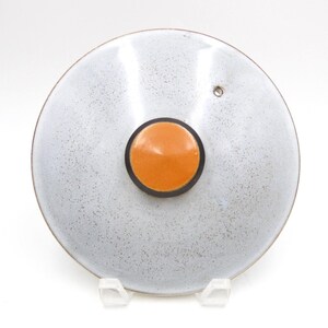 Peut inclure: Un couvercle de casserole circulaire avec une finition gris clair mouchetée et un bouton orange uni et lisse au centre. Le bouton est entouré d'un fin anneau noir, et un petit évent circulaire est situé près du bord de la surface du couvercle.