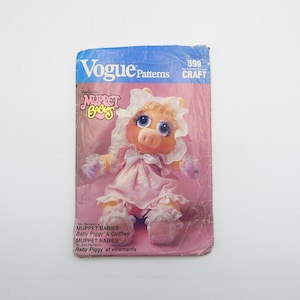 May include: A pink and white sewing pattern for a Miss Piggy doll. The pattern is from Vogue Patterns and is titled "Jim Henson's Muppet Babies™ Baby Piggy & Clothes".