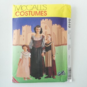 May include: McCall's Costumes sewing pattern number 8449 for a medieval costume. The pattern includes three sizes: large (16-18), grande, and taille. The pattern shows three people wearing the costumes: a woman and two girls. The woman is wearing a long, dark brown dress with a brown belt and a white collar. The girls are wearing long, pink dresses with white collars and brown belts. The background is a green field with a castle in the background.
