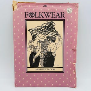 May include: A pink paper sewing pattern envelope for the Folkwear Armistice Blouse, pattern number 210. The front features a black and white illustration of three people holding an American flag, with the text Folkwear and Armistice Blouse printed.