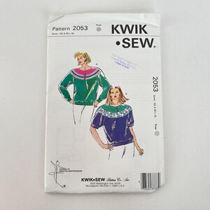 May include: A Kwik Sew sewing pattern, pattern number 2053, featuring illustrations of two different tops. The pattern includes sizes XS-XL. The package is white with the Kwik Sew logo and text.