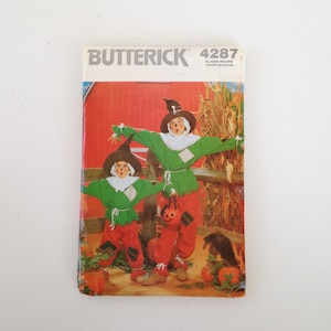 Puede incluir: Un patrón de costura Butterick vintage, número 4287, con una ilustración de dos disfraces de espantapájaros. Los disfraces son verdes, rojos y marrones, con una calabaza y un cuervo en el fondo. El patrón incluye todas las tallas.